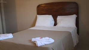 A neatly made bed with white linens and two pillows, a wooden headboard, and a folded towel on the bed. - Villa Rosa Hotel & Restaurant (Port-au-Prince)