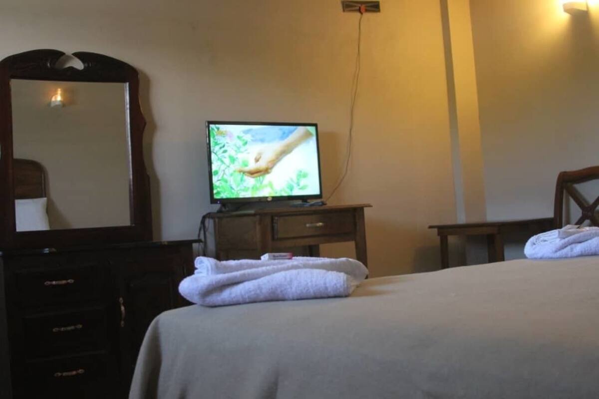 A hotel room with a bed, a television on a wooden stand, a mirror, and a wall socket.