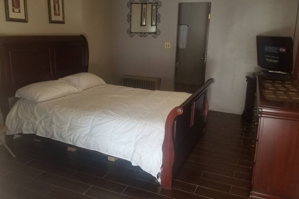 A bedroom with a wooden bed, a dresser, a mirror, and a television.