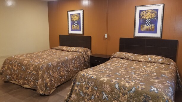 Ein Hotelzimmer mit zwei Betten, jeweils mit blumigem Bettbezug, Holzkopfteilen und zwei gerahmten Kunstwerken an den Wänden.