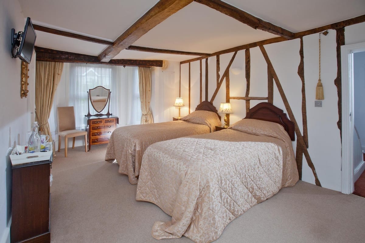 A bedroom with two beds, wooden beams, a dresser, a mirror, and a chair.