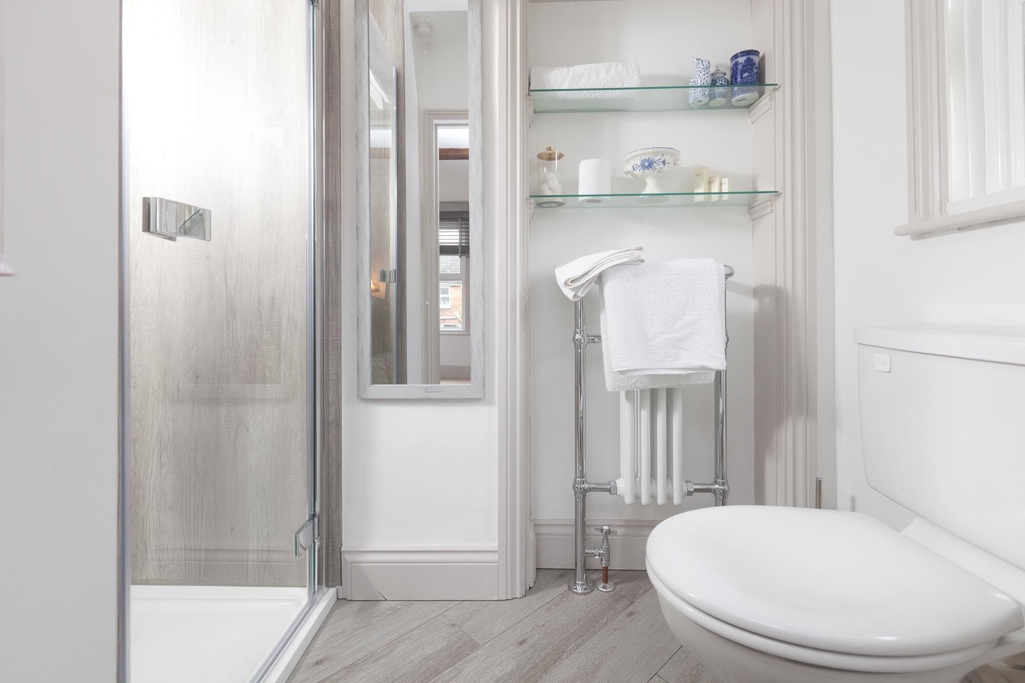 Une salle de bain moderne avec une douche à parois de verre, des toilettes blanches et une étagère en verre où sont rangés les articles de toilette.
