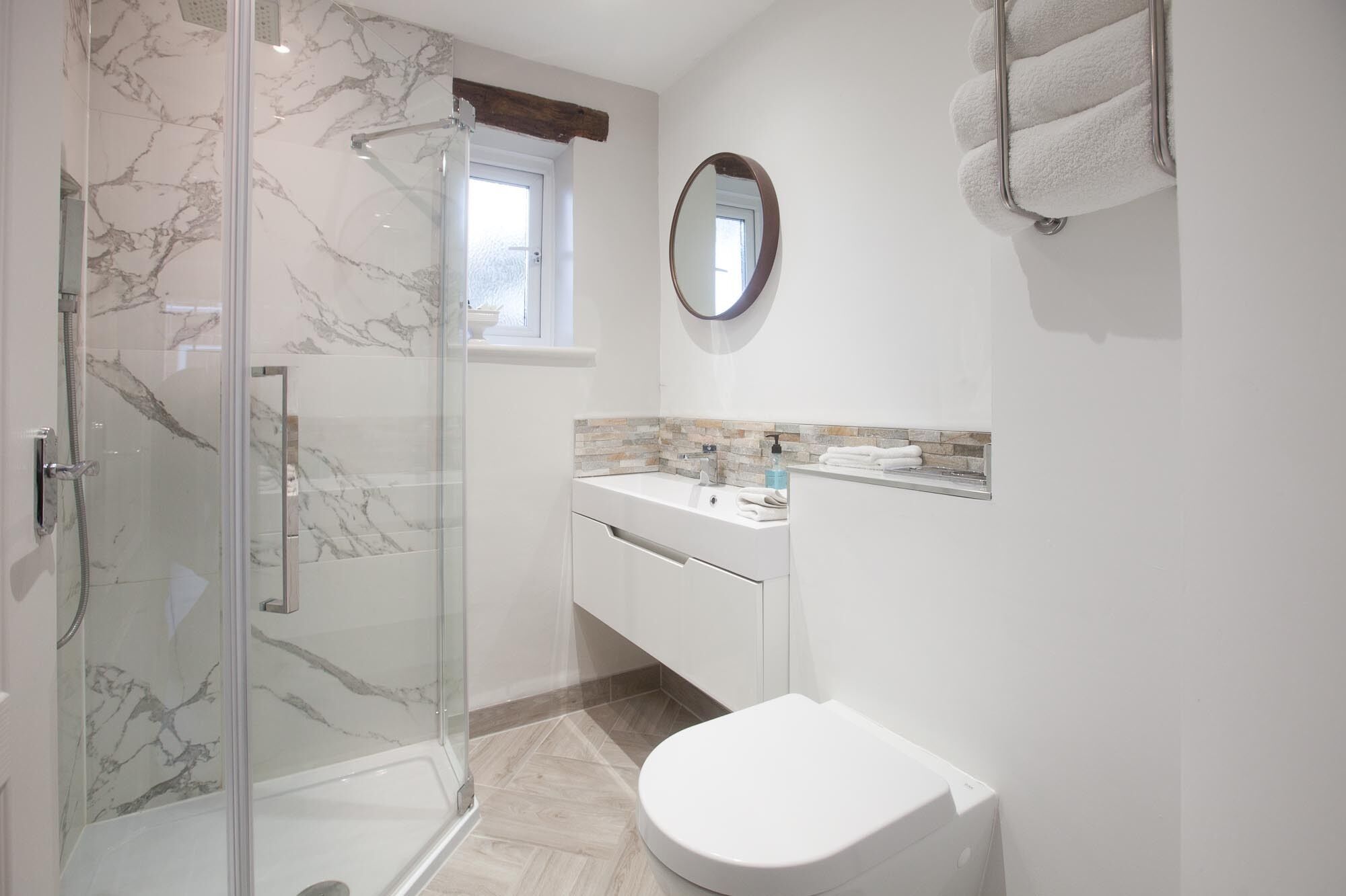 Un baño con cabina de ducha de vidrio, inodoro blanco, lavamanos con espejo y toallero.