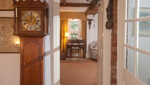 A room with a wooden floor, a desk with a lamp, a chair, and a large wall clock. - The Old House Guesthouse (Salisbury)