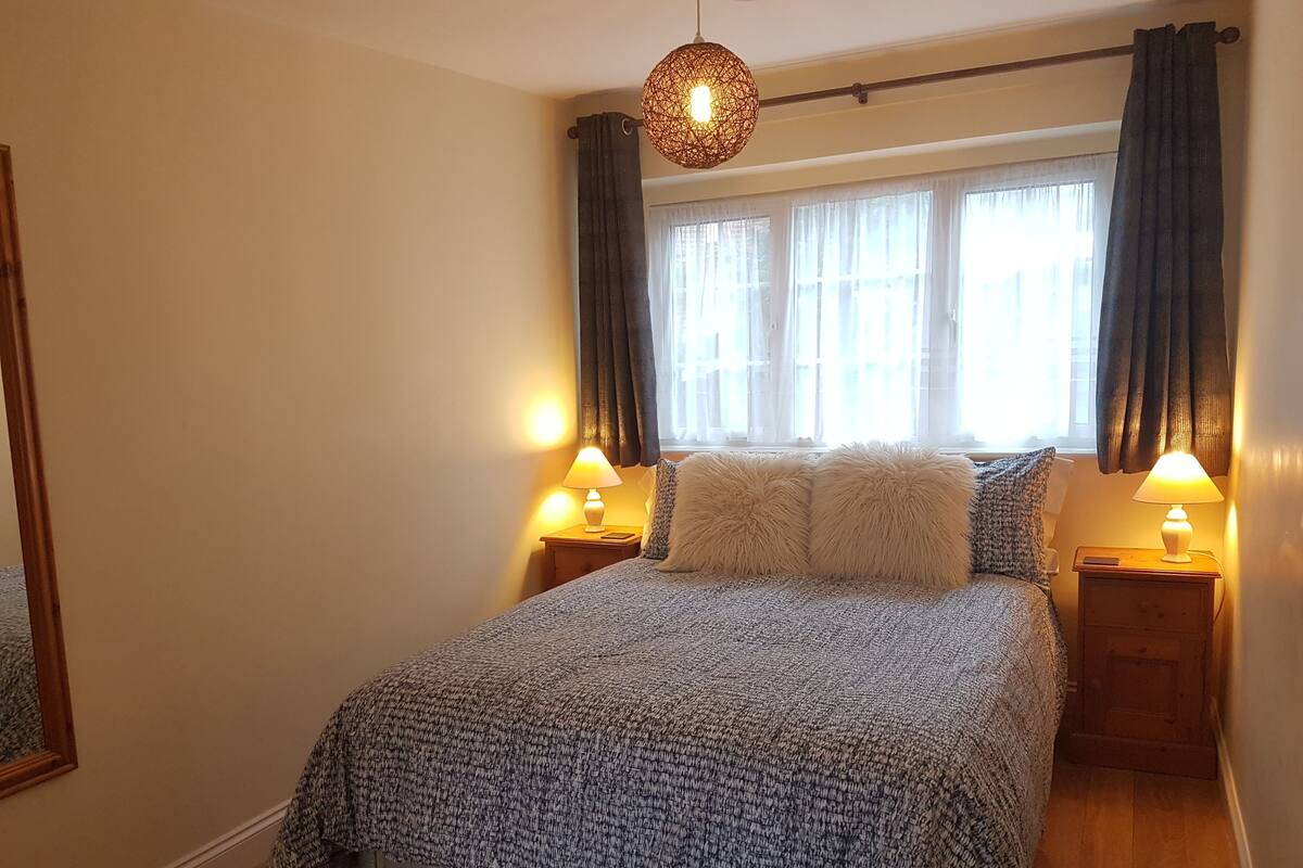 A neatly made bed with a patterned bedspread, two bedside lamps, and a hanging light fixture.