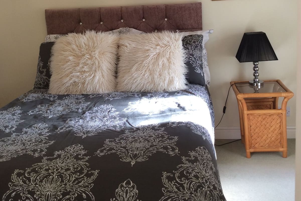 A bedroom with a tufted headboard, a bed with patterned bedding, a side table with a lamp, and a framed painting on the wall.
