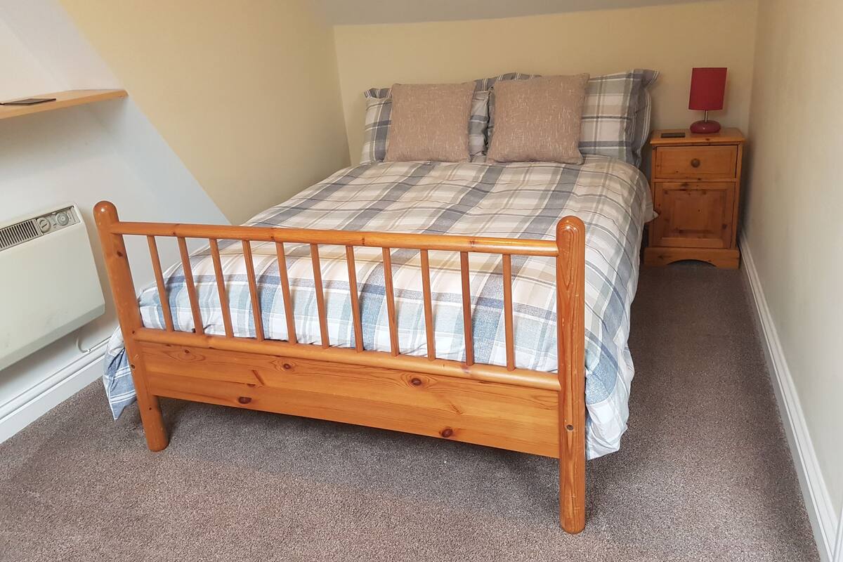 A bedroom with a wooden bed, a nightstand, a red lamp, and a wall-mounted shelf.