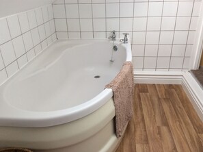A bathroom with a freestanding bathtub, white tiled walls, and wooden flooring. - Parkview Apartments (High Wycombe)