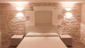 A bedroom with a stone wall, a large bed, and two bedside tables. - B&B il Castello (Giovinazzo)