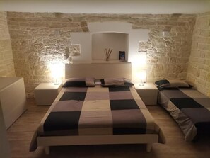 Un dormitorio con pared de piedra, una cama con colcha a cuadros, dos mesitas de noche con lámparas y un atril con un teléfono.