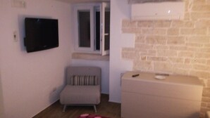 A small room with a television mounted on the wall, a window, a sofa, and a dresser. - B&B il Castello (Giovinazzo)