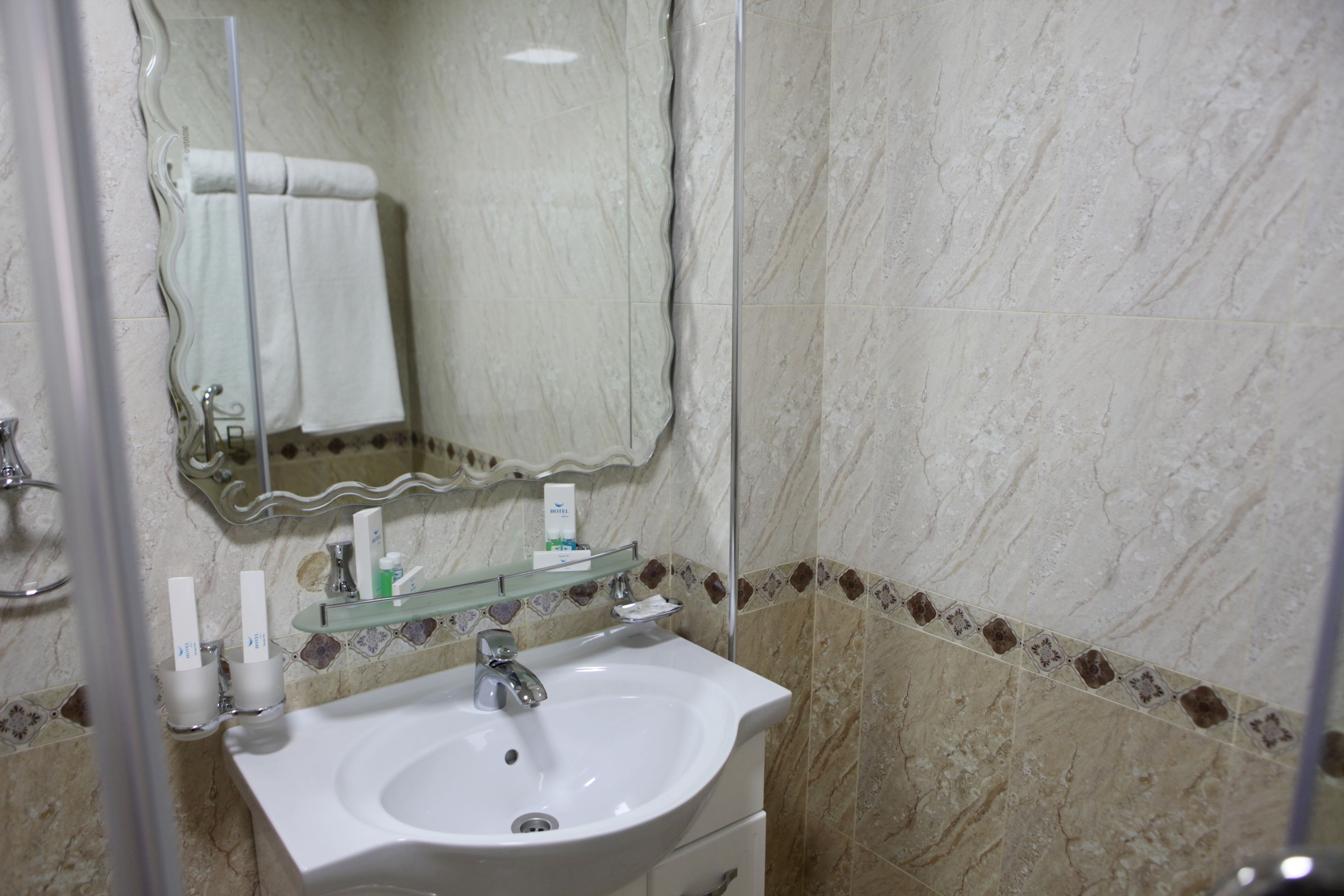 A bathroom with a white sink, a mirror, and a glass shelf with toiletries.