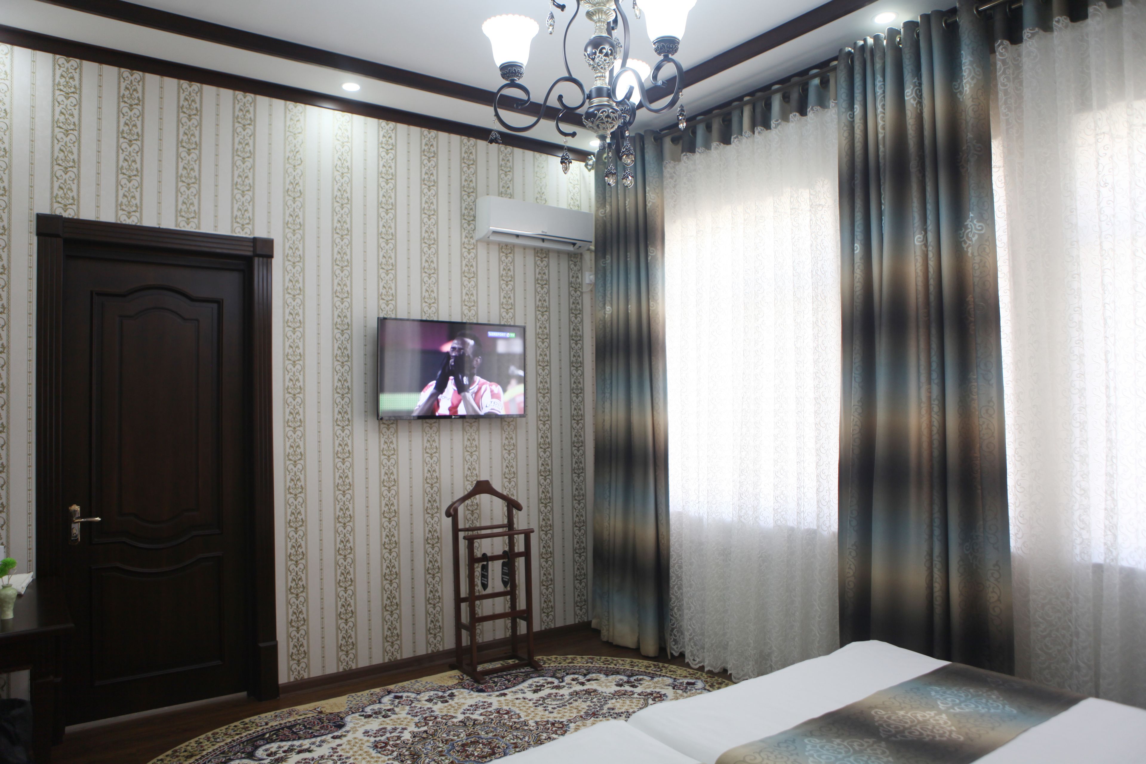 A hotel room with a large bed, a TV mounted on the wall, a wooden wardrobe, and a patterned carpet.