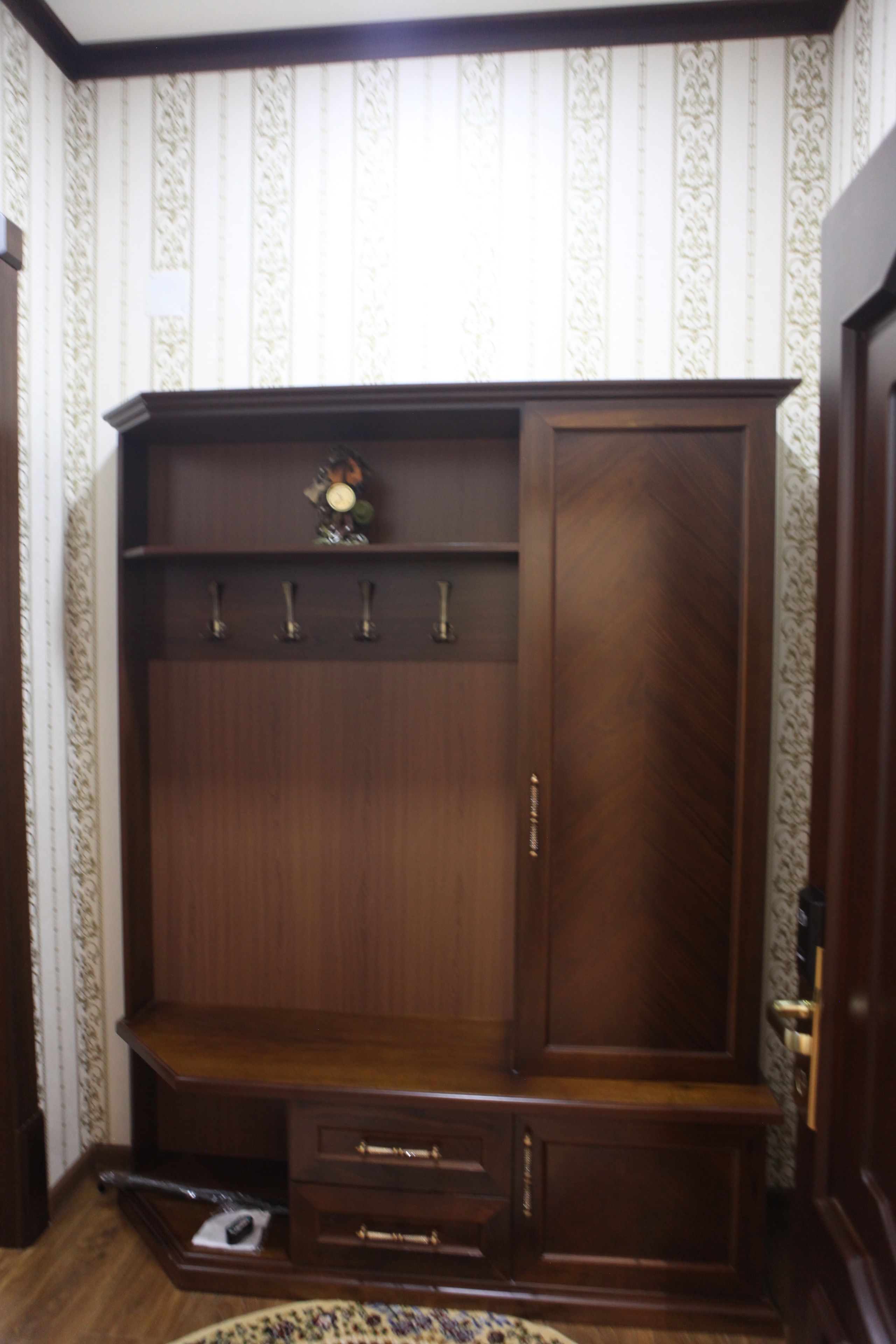 A wooden wardrobe with a mirror, a shelf, and a coat hook.