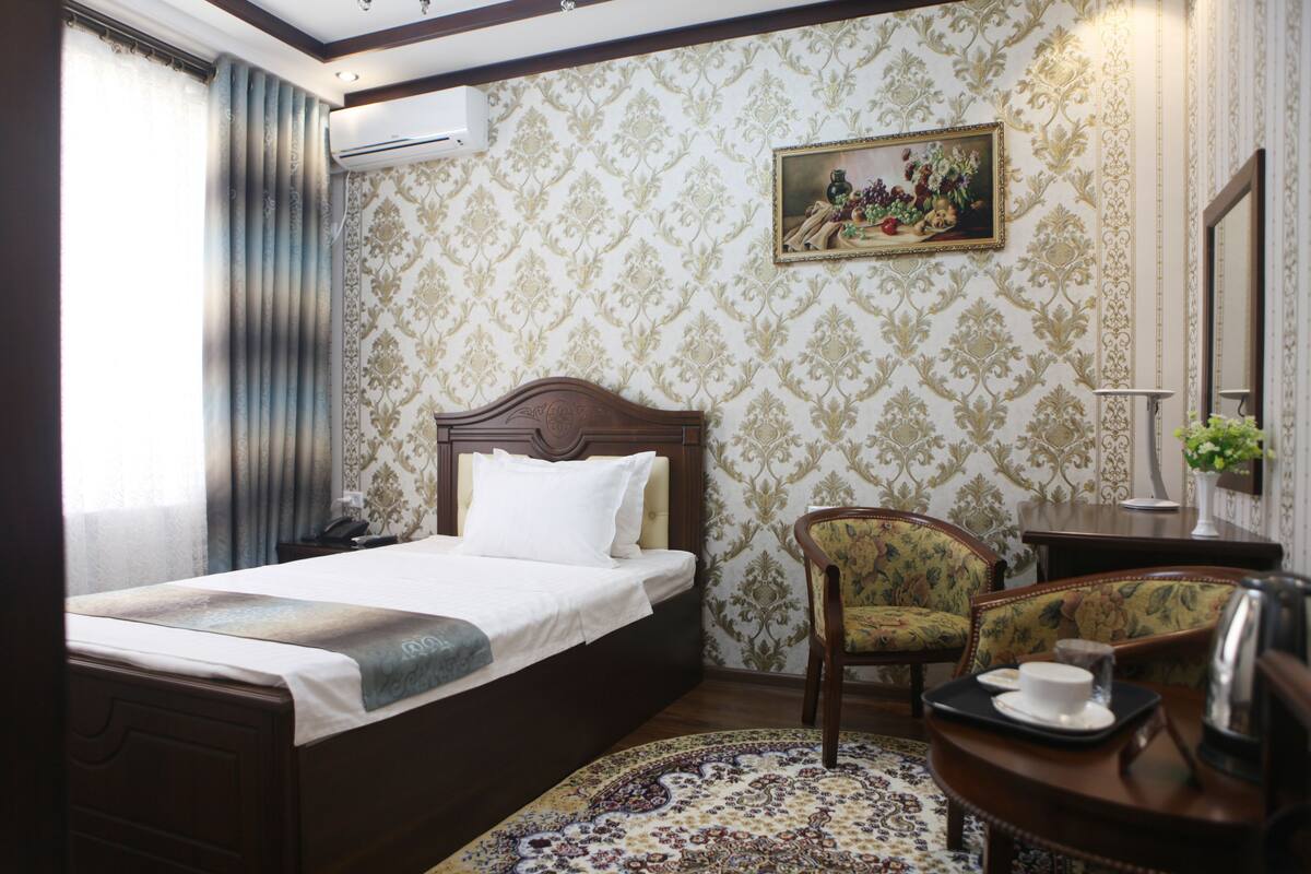 Ein Hotelzimmer mit Bett, Stuhl, Tisch mit Tasse und Untertasse sowie einem Gemälde an der Wand.