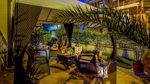 An outdoor patio area with wicker furniture, potted plants, and a guitar. - Hotel Corallo (Orbetello)