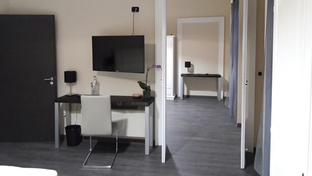A modern hotel room with a desk, a flat-screen TV, a small table, and a chair. There is a door leading to another room. - Bed and Breakfast La Mamma (Cittanova)