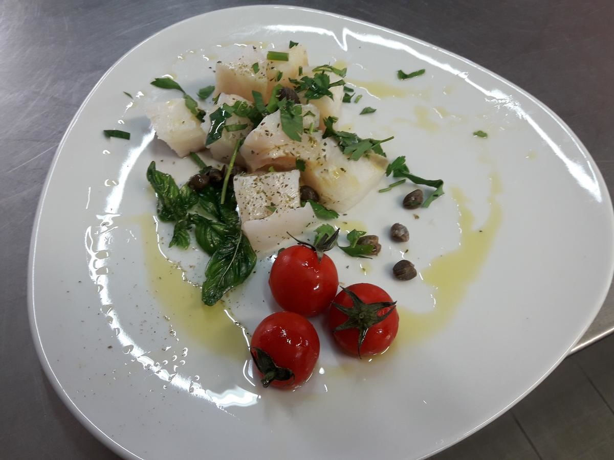 Une assiette blanche avec du poisson, des tomates cerises et des herbes aromatiques.