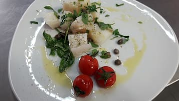 Ein weißer Teller mit Fisch, Kirschtomaten und Kräutern.