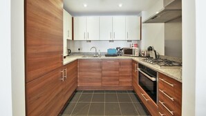 A compact kitchen with wooden cabinets, a gas stove, a microwave, and a sink. - 1Bed & 2Beds Apartment in Liverpool St by City Stay Aparts London (London)