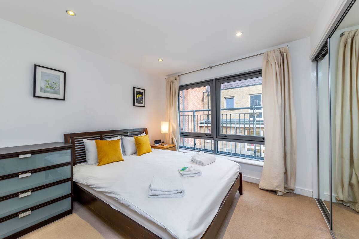 Een moderne hotelkamer met een groot bed, nachtkastjes, een dressoir en een raam met gordijnen.