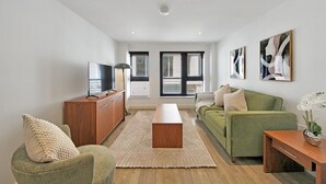 A modern living room with a green sofa, a wooden coffee table, and a flat-screen TV on a wooden cabinet. - 1Bed & 2Beds Apartment in Liverpool St by City Stay Aparts London (London)