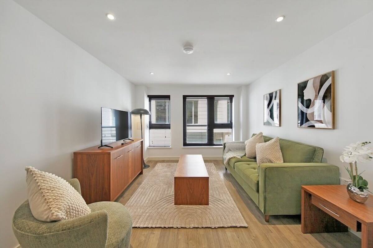 Een moderne woonkamer met een groene bank, een houten salontafel en een flatscreen televisie op een houten kast.