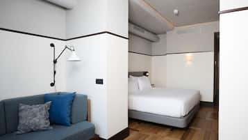 Quarto de hotel moderno com um sofá cinza, uma cama e uma mesa de cabeceira com abajur.