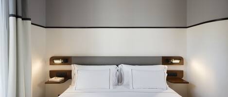 A modern hotel room with a neatly made bed, bedside tables, and built-in lighting.