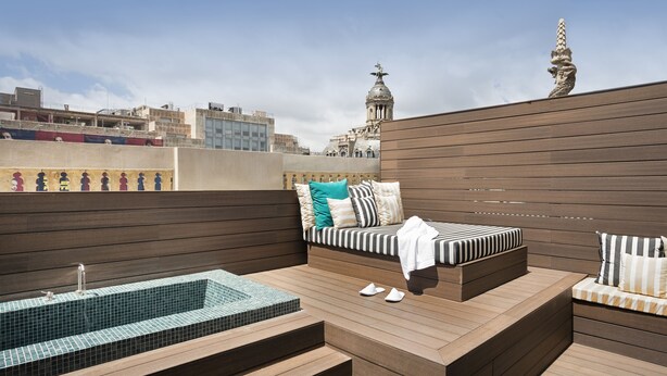 Una terrazza panoramica sul tetto con idromassaggio, zona relax con cuscini e vista sullo skyline della città.