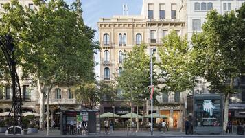 Vista de una calle con varios edificios, entre ellos un café llamado 'Oassis' y una tienda con un letrero que dice 'Mango Kid'.