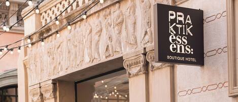 A boutique hotel entrance with a sign reading "PRAKTIK ESSENS: BOUTIQUE HOTEL".