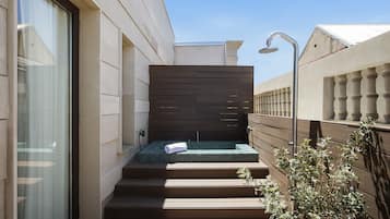 A modern outdoor spa area with a wooden deck, a small hot tub, and a showerhead.