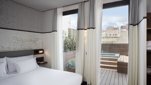 Camera d'albergo moderna con un letto grande, una testiera in legno, un comodino e vista sulla città attraverso ampie finestre.