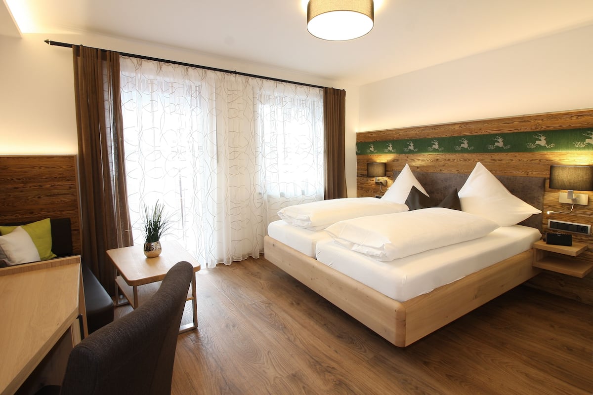 Ein Hotelzimmer mit einem hölzernen Bett, einem Schreibtisch, einem Stuhl und einem kleinen Tisch mit einer Pflanze.