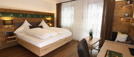 Habitación de hotel con una cama de madera, un escritorio con silla, una mesita pequeña y una planta en maceta.