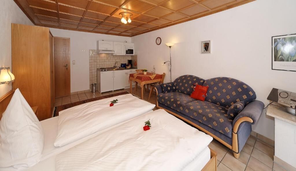 A bedroom with two beds, a sofa, a dining table, and a kitchenette.