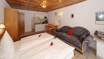 A bedroom with two beds, a sofa, a dining table, and a kitchenette.