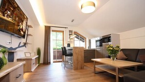 Un salon moderne avec un plancher en bois, un canapé noir, une table basse en bois et un téléviseur fixé au mur.