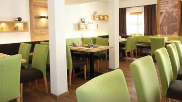 A restaurant with green upholstered chairs and tables, wooden accents, and pendant lighting.