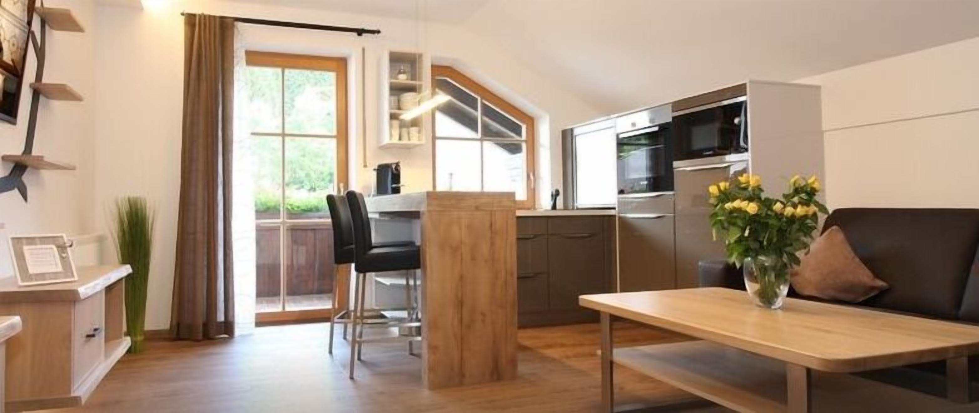 A modern kitchen with a dining area, a wooden table, and a sofa.