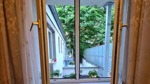 A room with a window overlooking a street, a radiator below the window, and curtains partially drawn. - Cara Vita Hotel (Cologne)