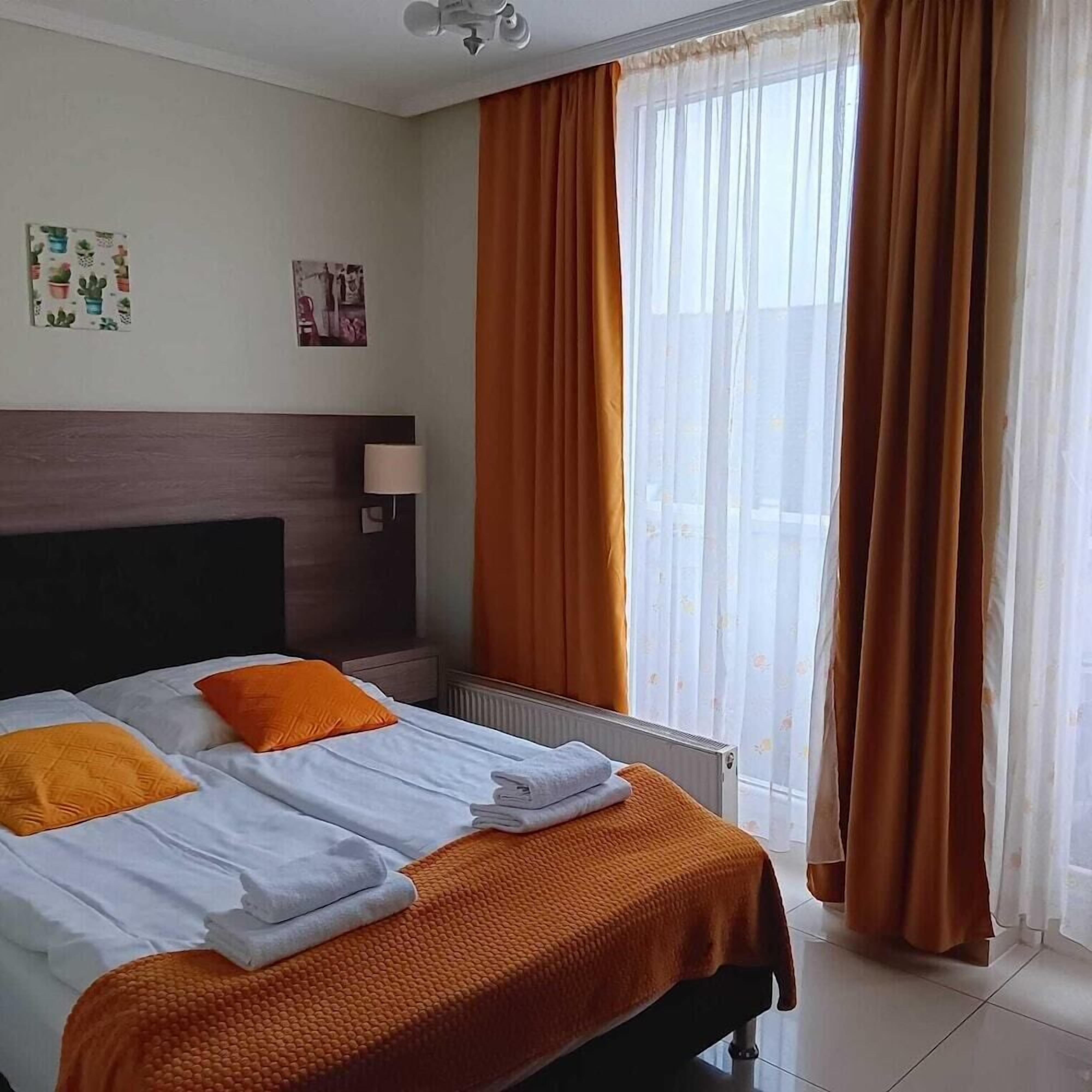 Quarto de hotel com cama, cabeceira, janela com cortinas e radiador.