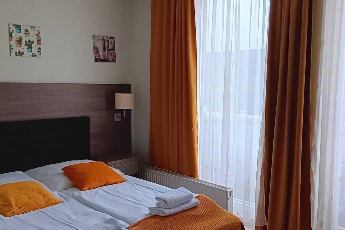A hotel room with a bed, a headboard, a window with curtains, and a radiator.