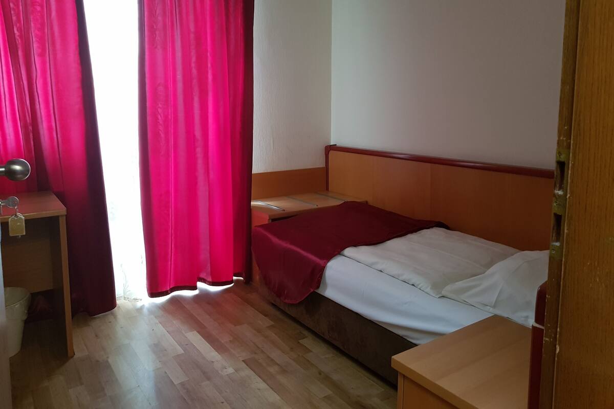 A room with a bed, a desk, and a window with red curtains.