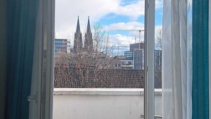 A view from a balcony with a cityscape, including tall buildings and a church with spires. - Cara Vita Hotel (Cologne)