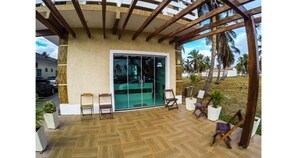 A covered outdoor area with a wooden ceiling, a glass door leading to a pool, and several chairs and potted plants. - Atalaia Vip Praia Hotel (Salinópolis)