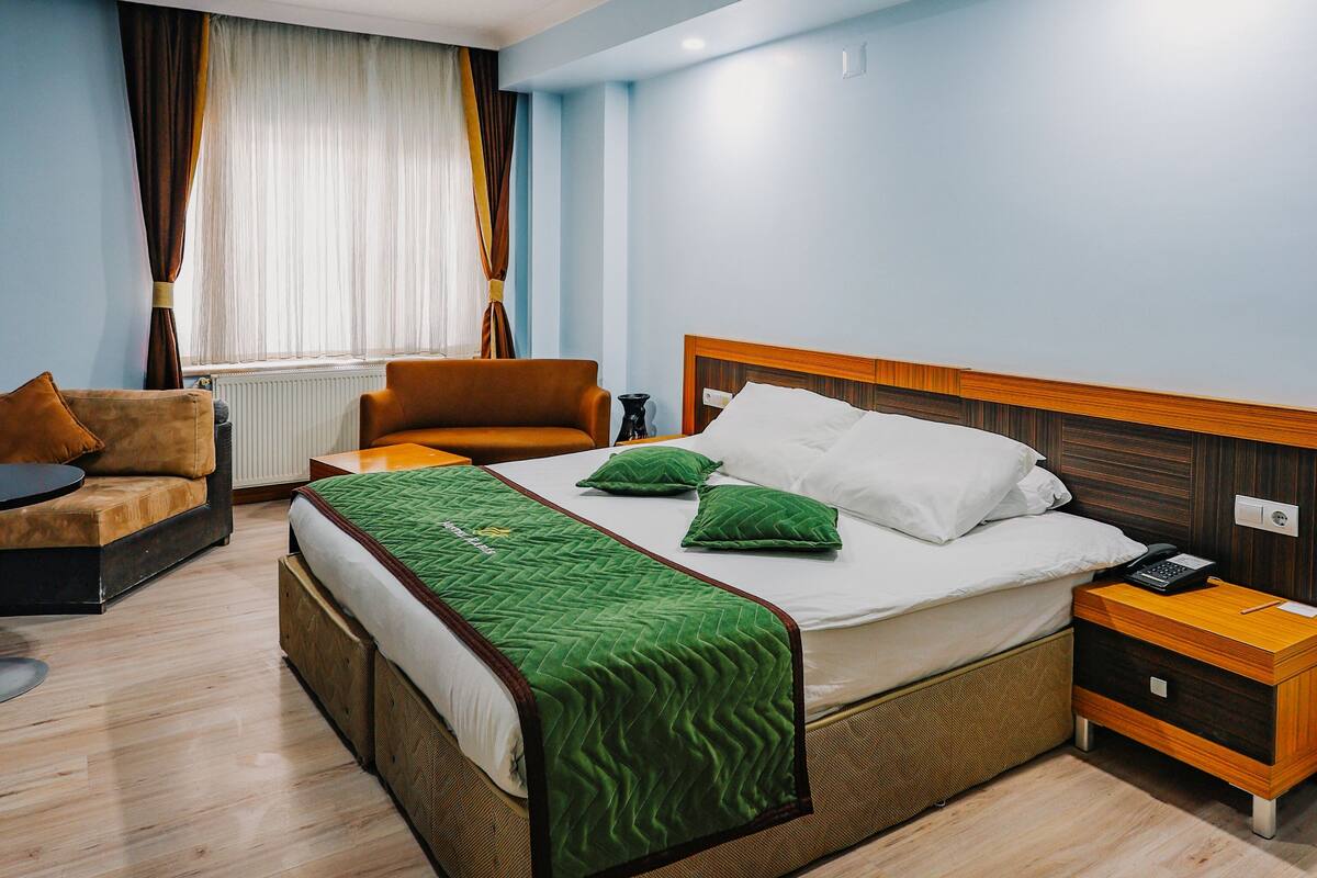 A hotel room with a bed, two chairs, a bedside table, a nightstand, and a window with curtains.