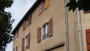 A two-story building with red shutters, a red door, and a small balcony. - Cafe Restaurant Meuble de Tourisme (Saint-Germain-de-Calberte)