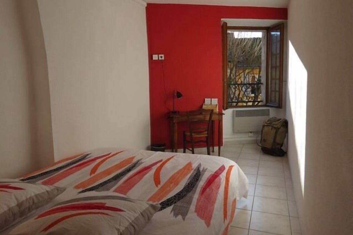 A bedroom with a bed, a desk, and a chair. There is a window with a view of the outside.